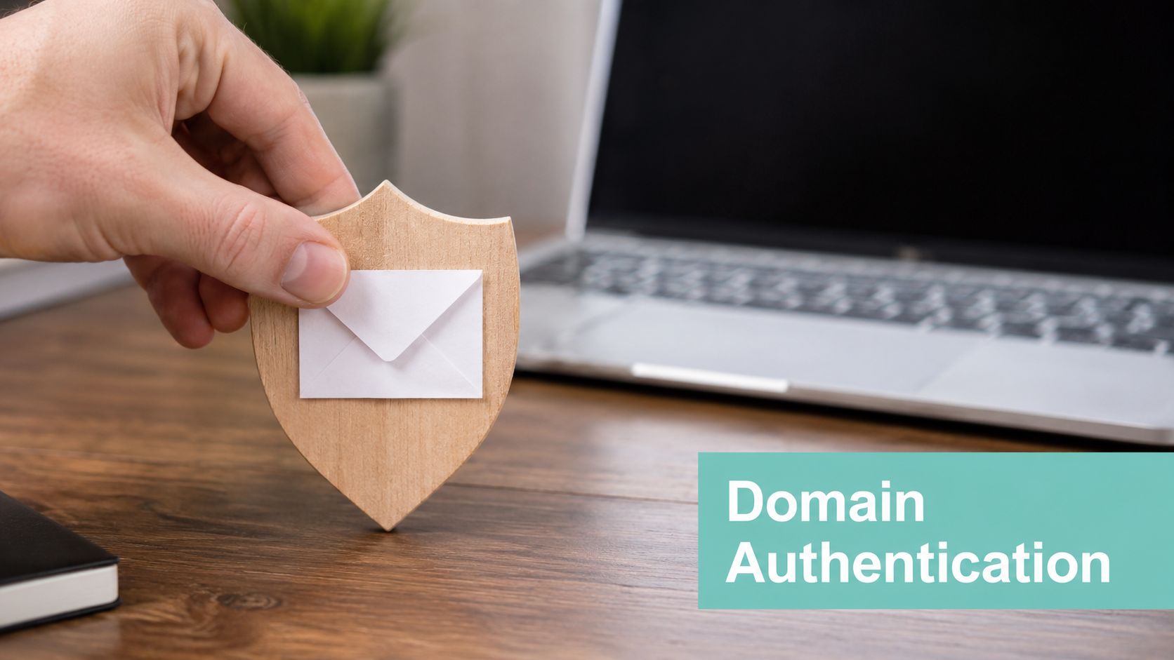 Safeguard Your Business: Email Security Best Practices 6 A hand holding a wooden shield icon with an envelope on a desk near a laptop